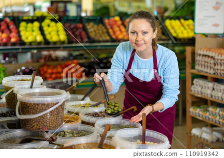 Middle-aged saleswoman showing olives in grocery store Middle-aged saleswoman showing olives in grocery store 110919342
