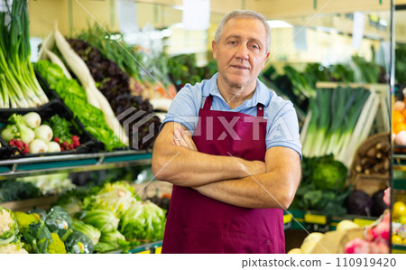 Portrait of confident mature male supermarket worker wearing apron standing in middle of grocery store Portrait of confident mature male supermarket worker wearing apron standing in middle of grocery store 110919420