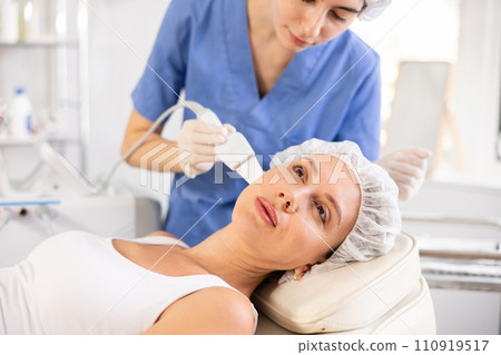 Young female client experiencing facial skin peeling using ultrasonic scrubber Young female client experiencing facial skin peeling using ultrasonic scrubber 110919517