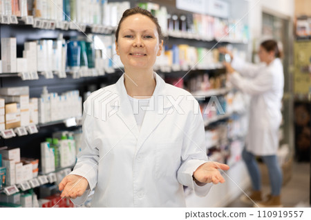 At pharmacy, apothecary waiting for customers and invites with gesture go to department of cosmetics 110919557