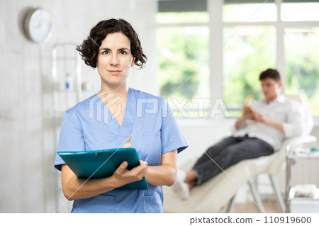 Middle-aged woman doctor posing in doctor's cabinet with document in hands Middle-aged woman doctor posing in doctor's cabinet with document in hands 110919600