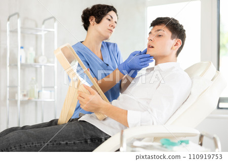 Beautician woman using mirror consulting man in clinic Beautician woman using mirror consulting man in clinic 110919753