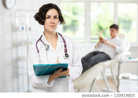 Middle-aged woman doctor posing in doctor's cabinet with document in hands 110919803