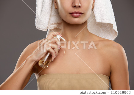 After shower body care. Cropped image of woman in towel applying body oil for glow and nourishing effect against studio background After shower body care. Cropped image of woman in towel applying body oil for glow and nourishing effect against studio background 110919963