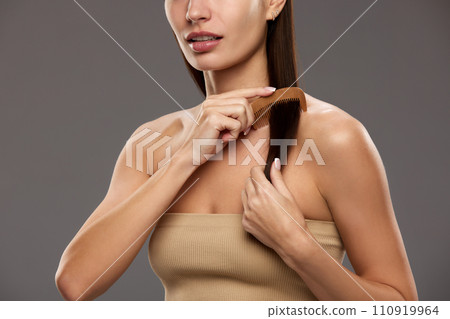 Cropped image of woman taking care after hair, brushing, applying special hair products for moisturizing against studio background 110919964