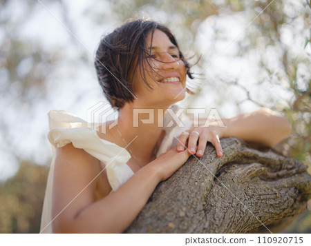 Beautiful Asian young woman in white dress outdoor near olive tree. embracing fresh air and engaging in outdoor activities. Friluftsliv concept means spending as much time outdoors as possible Beautiful Asian young woman in white dress outdoor near olive tree. embracing fresh air and engaging in outdoor activities. Friluftsliv concept means spending as much time outdoors as possible 110920715