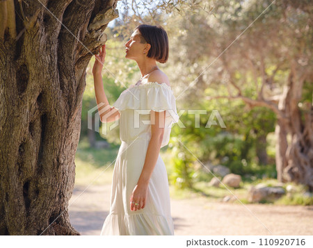 Beautiful Asian young woman in white dress outdoor near olive tree. embracing fresh air and engaging in outdoor activities. Friluftsliv concept means spending as much time outdoors as possible Beautiful Asian young woman in white dress outdoor near olive tree. embracing fresh air and engaging in outdoor activities. Friluftsliv concept means spending as much time outdoors as possible 110920716