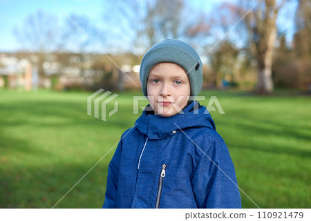 Young Autumn Explorer: Beautiful 8-Year-Old Boy in Jacket and Beanie Standing in the Park with Green Lawn Young Autumn Explorer: Beautiful 8-Year-Old Boy in Jacket and Beanie Standing in the Park with Green Lawn 110921479