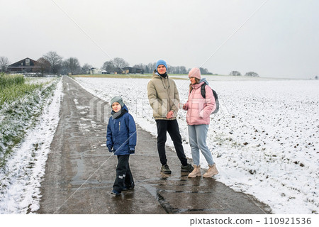 Winter Family Bliss: Mother and Two Sons Enjoying a Snowy Countryside Stroll. Winter, Snow, Mother, Two sons, Family, Rural road, Snow-covered field, Winter landscape 110921536