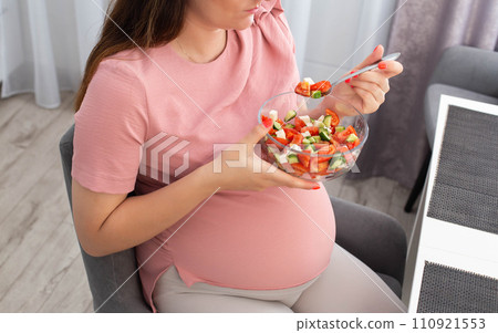 Pregnant girl eats vegetable salad in the kitchen. The concept of proper nutrition rich in vitamins during pregnancy. Healthy food. Hemoglobin increase 110921553