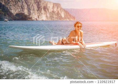 Woman sup sea travel. Sports girl on a surfboard in the sea on a sunny summer day. In a black bathing suit, he sits on a sapa in the sea. Rest on the sea. 110921917