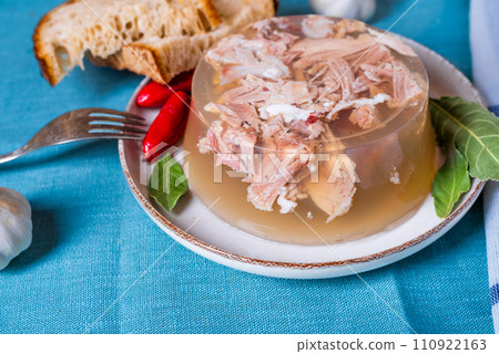 Jelly with meat, beef aspic, traditional dish. portion on plate. Bread and chili. 110922163