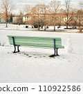 A small snowman beside the green bench in the snow park 110922586