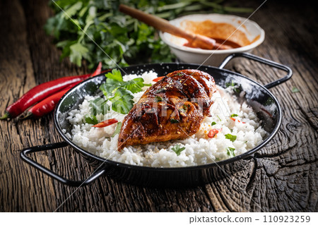 Grilled chicken breast served in a pan with jasmine rice and chili peppers Grilled chicken breast served in a pan with jasmine rice and chili peppers 110923259