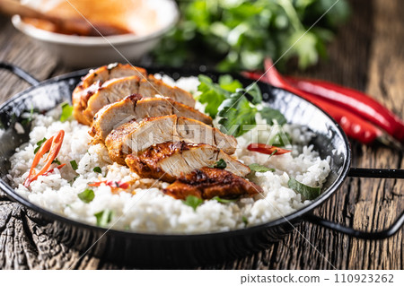 Grilled chicken breast served in a pan with jasmine rice and chili peppers Grilled chicken breast served in a pan with jasmine rice and chili peppers 110923262