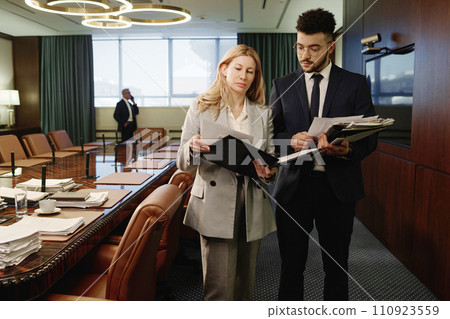 Female lawyer and her young male colleague reading papers, their coworker having call on background 110923559