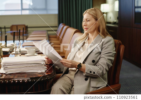 Experienced business woman reading document from pile of papers placed on table in conference room 110923561