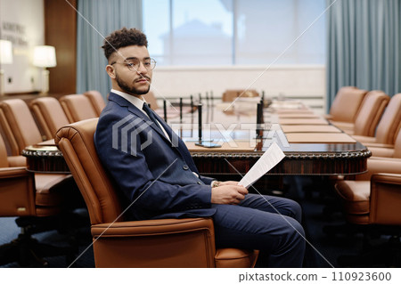 Lawyer in business suit sitting in armchair in boardroom with document in hands looking at camera Lawyer in business suit sitting in armchair in boardroom with document in hands looking at camera 110923600