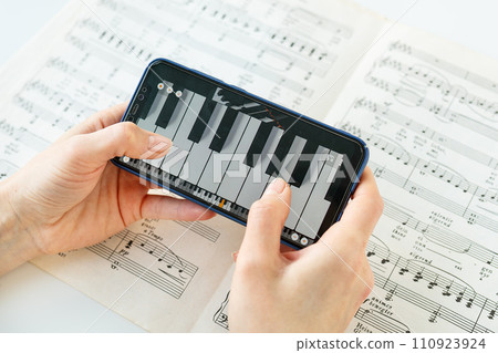 This image shows a person s hands holding a smartphone displaying piano keys over a sheet of musical notes. The image is bright and clear. 110923924
