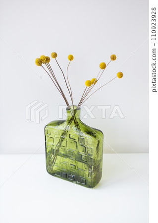 A green textured glass vase with yellow Craspedia flowers against a white background. Simple and elegant. A green textured glass vase with yellow Craspedia flowers against a white background. Simple and elegant. 110923928