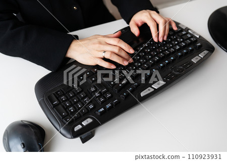 A girl in a black outfit typing on a full-sized black keyboard with a mouse. The keyboard has various function keys and multimedia buttons visible. A girl in a black outfit typing on a full-sized black keyboard with a mouse. The keyboard has various function keys and multimedia buttons visible. 110923931