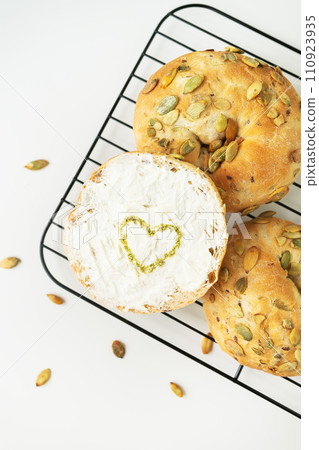 Freshly baked seed rolls on a cooling rack, one with a heart drawn in spices on cream cheese. 110923935