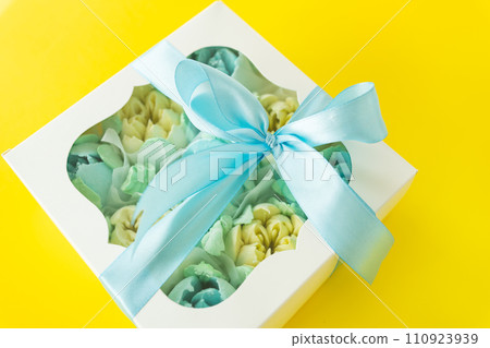 Colorful flower arrangement in a white gift box with a window. A bright blue satin ribbon is tied around the box with an elegant bow. 110923939