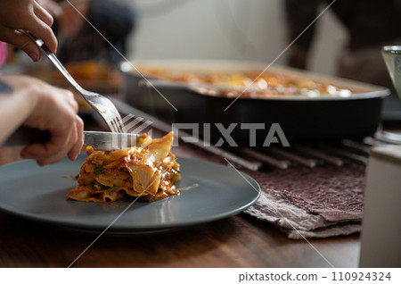 Closeup view of a childs hands cutting delicious homemade vegan vegetable lasagna Closeup view of a childs hands cutting delicious homemade vegan vegetable lasagna 110924324