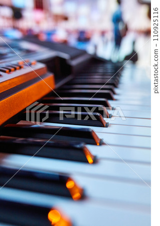 Close-up of piano keys with blurred silhouettes of people in background. Promotional material for a community outdoor piano project. Close-up of piano keys with blurred silhouettes of people in background. Promotional material for a community outdoor piano project. 110925116