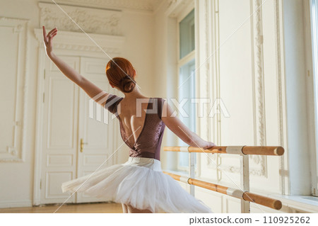 Young ballerina in tutu skirt stretching practicing ballet positions near ballet barre in dance class. Young classical dancer woman in dance studio. Ballet class training. Ballet school concept 110925262