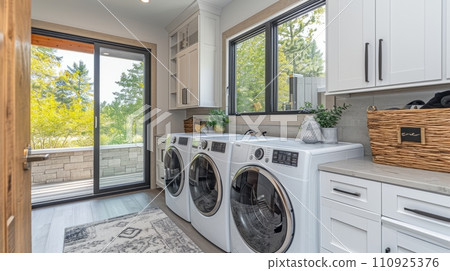 AI-generated content. Interior of elegant laundry room in a modern house. White wooden cabinets, marble tabletop, washing machine and dryer, large windows. 110925376