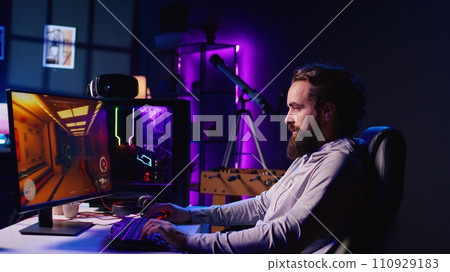 Pro gamer competing in intense online multiplayer videogame, shooting enemies with futuristic gun from living room with rgb lights. Panning shot of man using gaming computer to play internet game 110929183