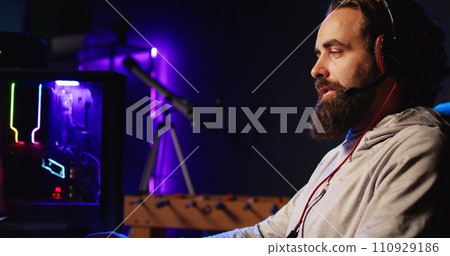Man relaxing by playing science fiction FPS videogame with friends on PC in RGB lit apartment late at night. Happy gamer talking with teammates, shooting enemies in online multiplayer shooter 110929186