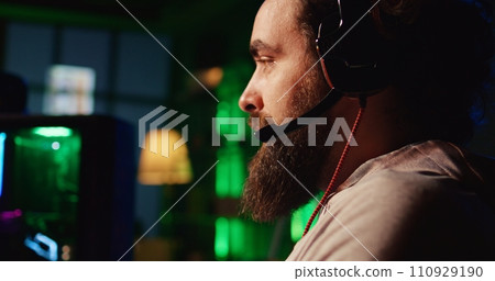Man playing FPS videogame with friends, talking through headphones mic, close up shot. Gamer competing in PvP online multiplayer game with teammates, shooting enemies with futuristic gun 110929190