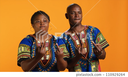 Rude ethnic couple showing middle finger in studio, doing offensive provocative gesture over orange background. Furious violent man and woman starting fight, negative hooligan symbol. Rude ethnic couple showing middle finger in studio, doing offensive provocative gesture over orange background. Furious violent man and woman starting fight, negative hooligan symbol. 110929264