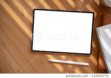 Top view image of a digital tablet mockup on a wooden table with a tablet pen and stationery. 110930770