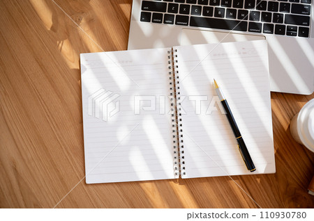 Top view of a wooden table with an opened book, a pen, a laptop computer, and a coffee cup. Top view of a wooden table with an opened book, a pen, a laptop computer, and a coffee cup. 110930780