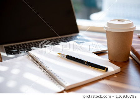 A wooden table with an opened book, a pen, a laptop, and a coffee cup. workspace in a cafe concept 110930782