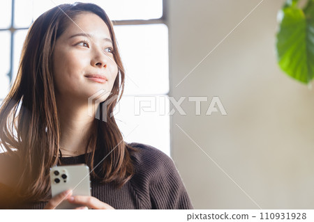A woman relaxing with a smartphone in her room A woman relaxing with a smartphone in her room 110931928
