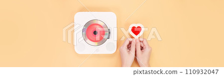 Hands holding heart shape red gift card next to white cd player with red disc on yellow background. Love music, Valentine day, Greeting, retro Love song, space for text. Hands holding heart shape red gift card next to white cd player with red disc on yellow background. Love music, Valentine day, Greeting, retro Love song, space for text. 110932047