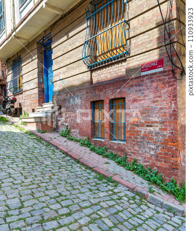 Turkey's timeless beauty: Istanbul's Balat district. Sun-drenched red brick building in a narrow cobblestone lane Turkey's timeless beauty: Istanbul's Balat district. Sun-drenched red brick building in a narrow cobblestone lane 110933923