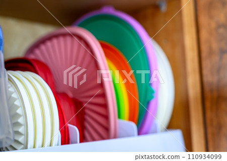 Narrow depth of field picture of an open kitchen cabinet with rows of organized storage of plastic lids. 110934099