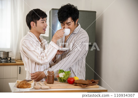 Happy gay couple enjoy breakfast in kitchen drinking coffee. Two best friends LGBTQ relation partner home cooking. Happiness romance homosexual marriage lifestyle. Two men together love friendship. Happy gay couple enjoy breakfast in kitchen drinking coffee. Two best friends LGBTQ relation partner home cooking. Happiness romance homosexual marriage lifestyle. Two men together love friendship. 110934307
