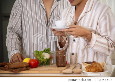 Happy gay couple enjoy breakfast in kitchen drinking coffee. Two best friends LGBTQ relation partner home cooking. Happiness romance homosexual marriage lifestyle. Two men together love friendship. Happy gay couple enjoy breakfast in kitchen drinking coffee. Two best friends LGBTQ relation partner home cooking. Happiness romance homosexual marriage lifestyle. Two men together love friendship. 110934308
