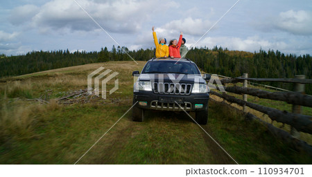 Hikers standing up through sunroof of car laugh and wave hands 110934701