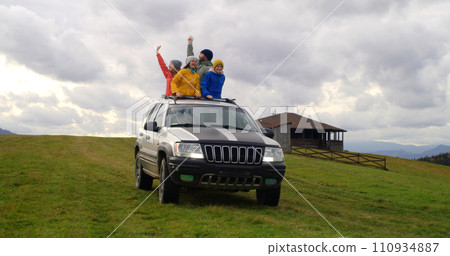 Hikers standing up through sunroof of car dance and wave hands Hikers standing up through sunroof of car dance and wave hands 110934887