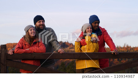 Multiethnic couples stand near wooden fence, look at beautiful sunset Multiethnic couples stand near wooden fence, look at beautiful sunset 110934987
