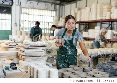 Female sculptor having ceramics in hands and standing in workroom 110936453