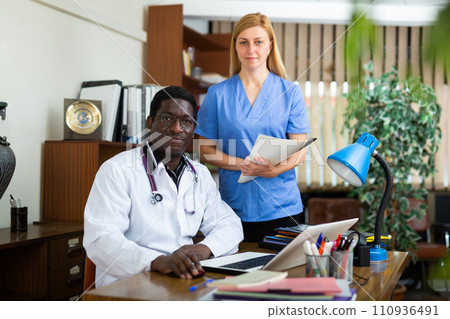 Experienced african american doctor sitting in office with female colleague 110936491