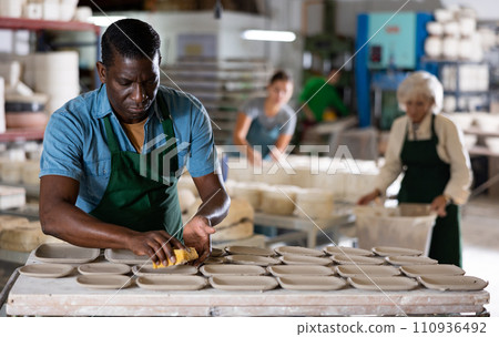 African american man prepares pottery with foam sponge - removes roughness and unevenness 110936492